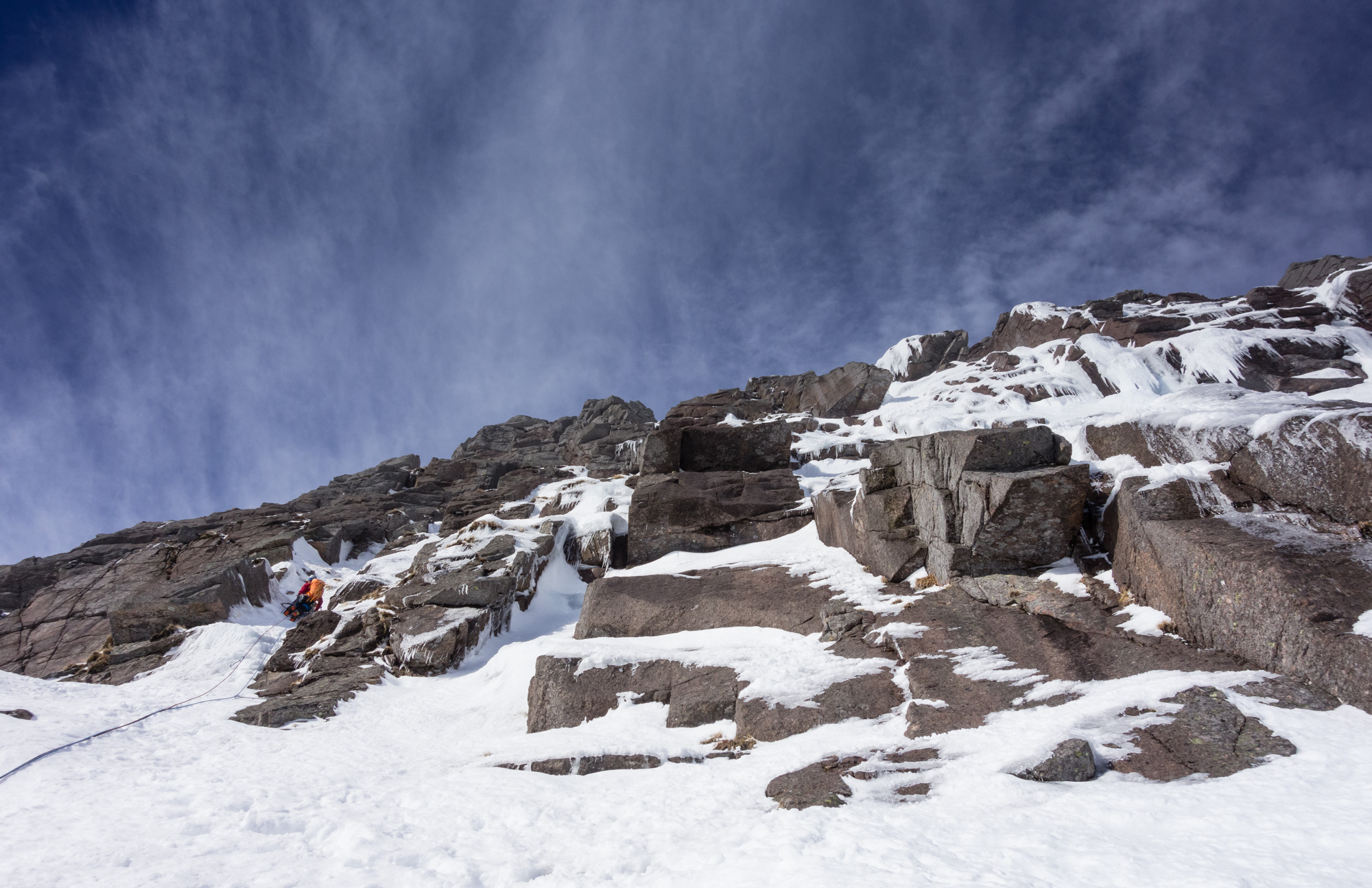 Andy begins 150 m of perfect neve and ice climbing while cloud and spindrift stream off the plateau above in the strong winds.